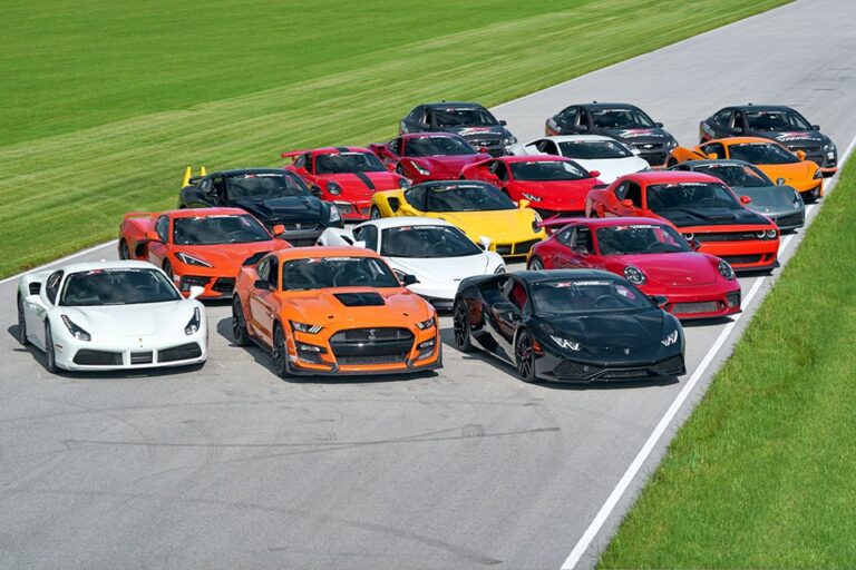 A lineup of colorful sports cars parked on a race track, with green grass beside the asphalt.